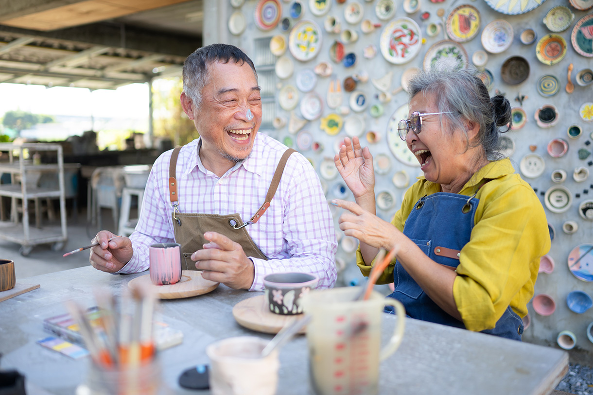 An older couple smiling and painting pottery.